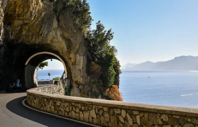 The coast road on the Amalfi Coast, curving into a tunnel cut through the rock above the sea.