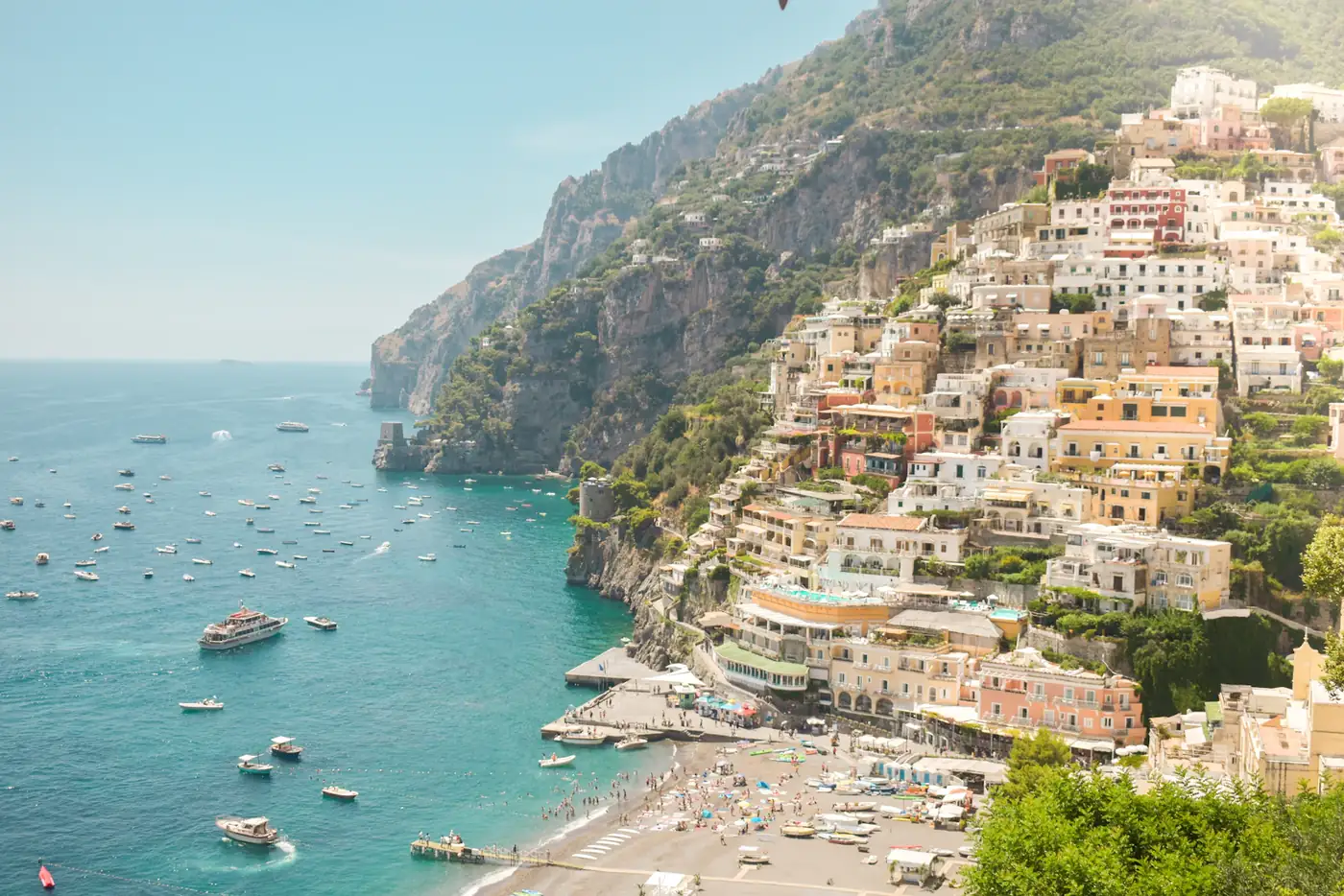 Positano’s houses stacked up the cliff above a beach and a bay full of boats.